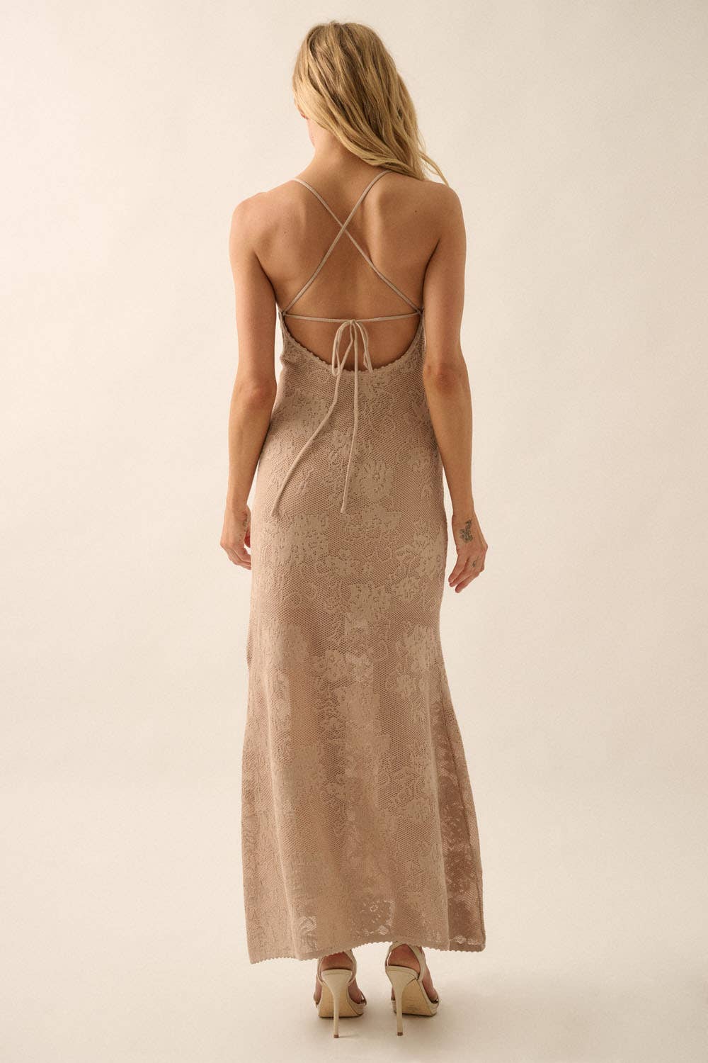 Woman wearing a sheer white lace maxi dress with spaghetti straps and floral detailing.