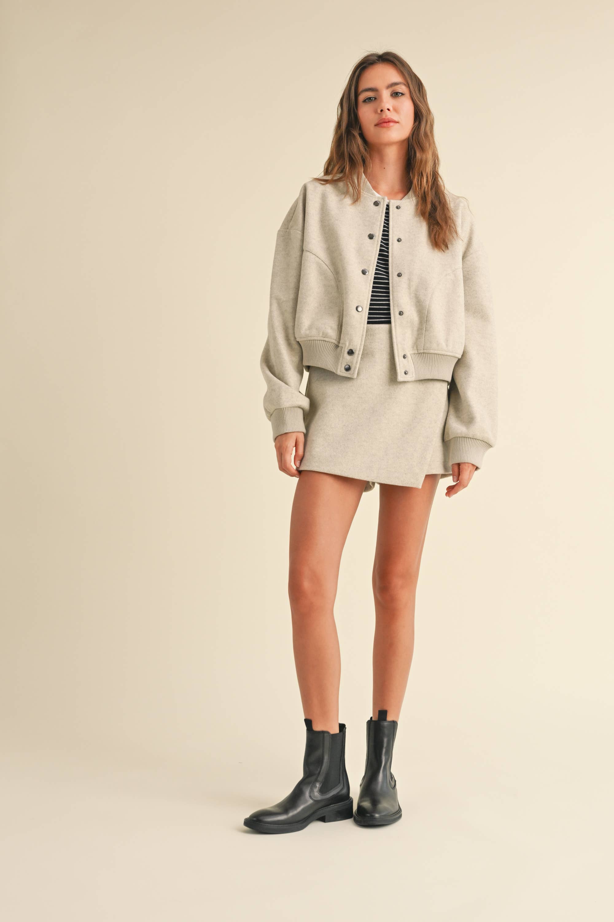 Model wearing a wool-blend jacket and mini skirt set in a neutral tone, styled with a striped tee and relaxed fit, showcasing casual elegance.