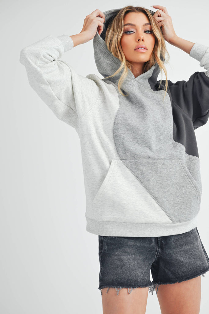 Woman wearing an oversized colorblock hoodie in grey, black, and ivory with a relaxed fit and kangaroo pocket.