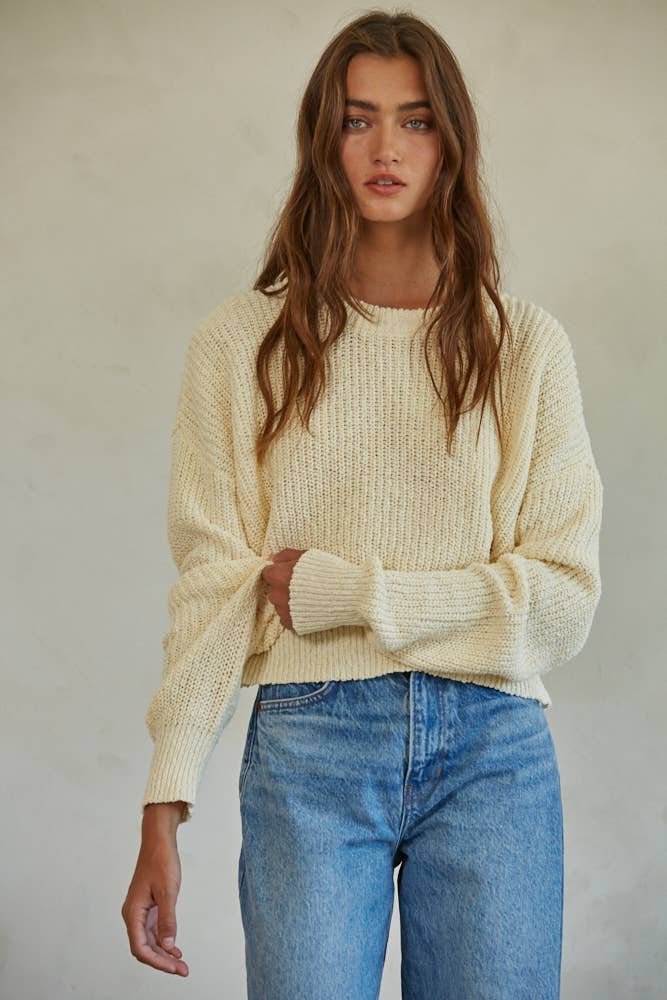 Woman wearing a cream chunky knit pullover sweater with relaxed fit, styled casually with light-wash jeans.