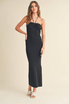 Model wearing a black halter dress with a twisted front detail, standing confidently with wavy hair.