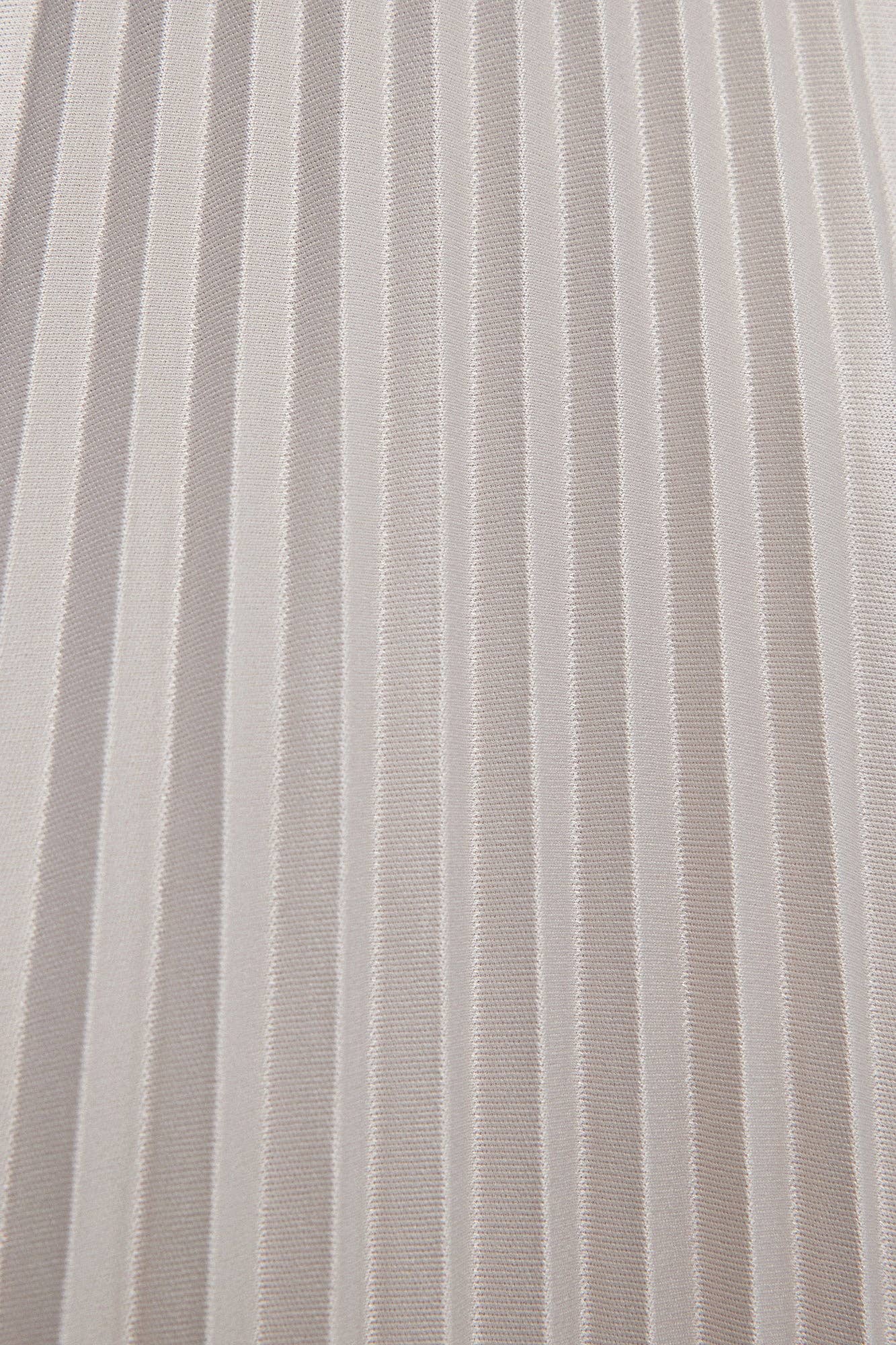 Model wearing a high-waisted pleated maxi skirt styled with a white blouse and pointed heels.