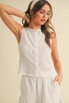 Model wearing a white sleeveless textured two-piece set featuring a cropped top and matching shorts with pockets.