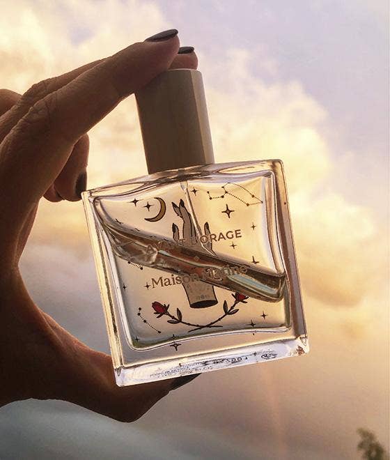 Maison Matine Avant l’Orage perfume bottle with celestial illustrations, placed among citrus fruits and sample vials on blue fabric