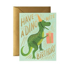 A birthday card featuring a green dinosaur wearing a party hat and holding a gift, with the text "Have a Dino-Mite Birthday," paired with a gold envelope.