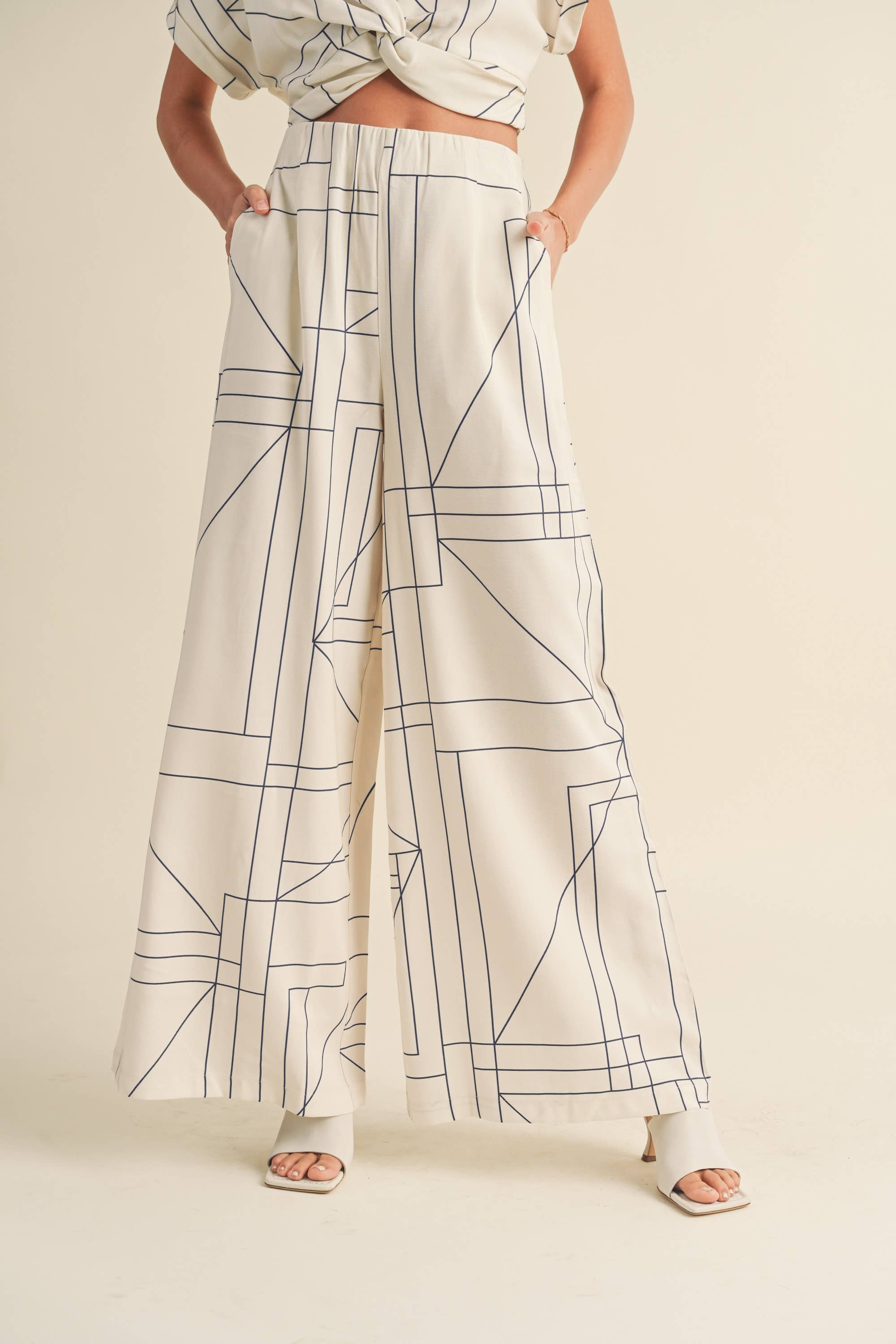 Woman wearing a cream two-piece set with geometric line print, knotted crop top, and wide-leg pants.