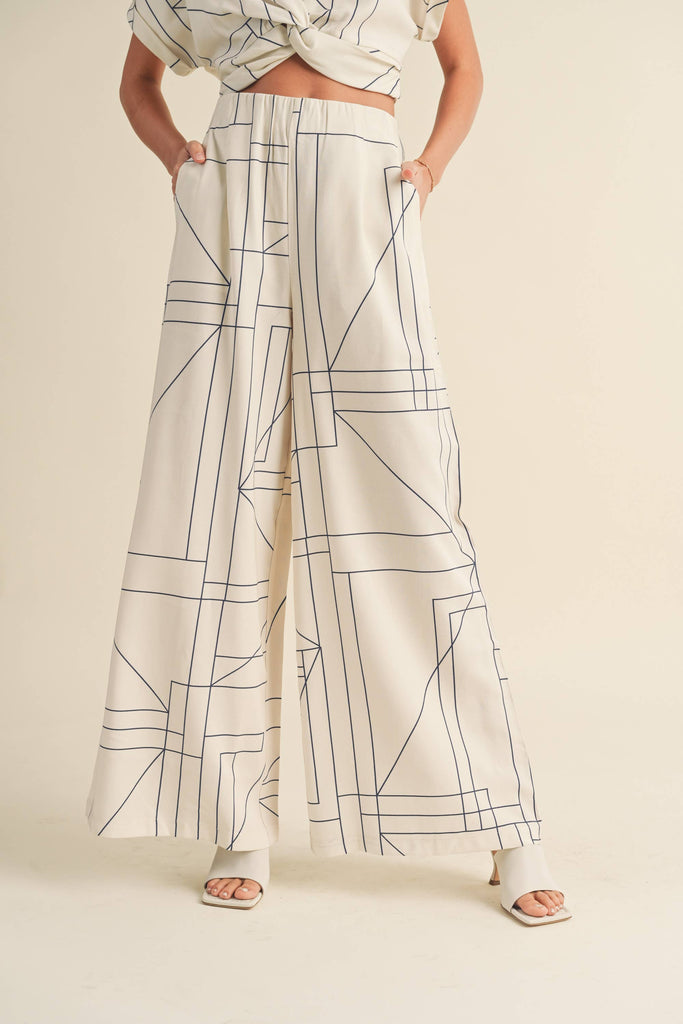 Woman wearing a cream two-piece set with geometric line print, knotted crop top, and wide-leg pants.