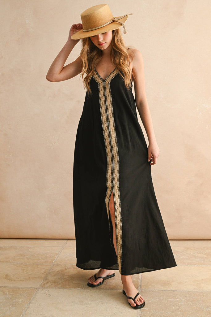 Model in black embroidered maxi dress with thin straps and flowy silhouette, featuring beige V-shaped stitching detail.