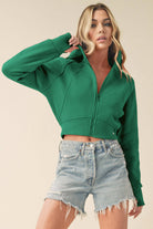 Model wearing a cropped zip-up hoodie with adjustable hood and ribbed cuffs, paired with distressed denim shorts.