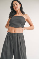 Woman wearing a strapless navy pinstriped crop top with tailored pleated pants.