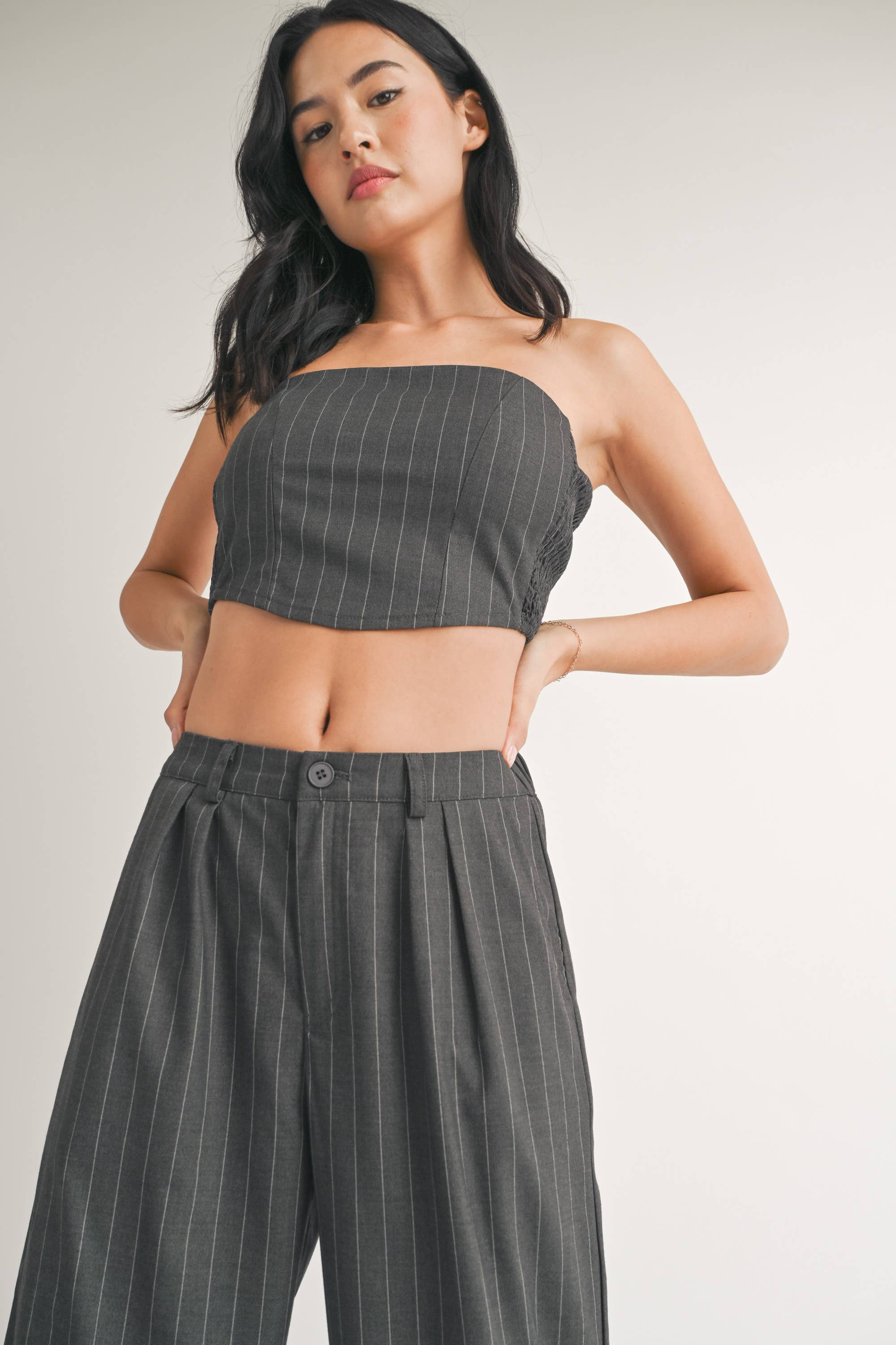 Woman wearing a strapless navy pinstriped crop top with tailored pleated pants.