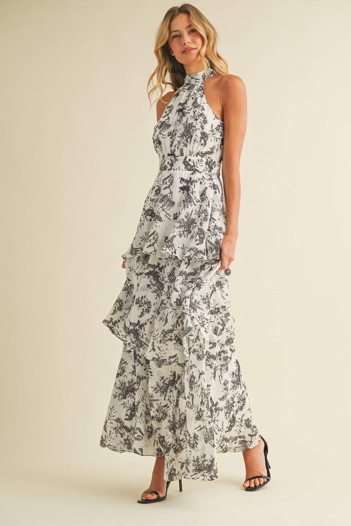 Woman wearing a halter neck tiered maxi dress with black floral print and ruffle layers
