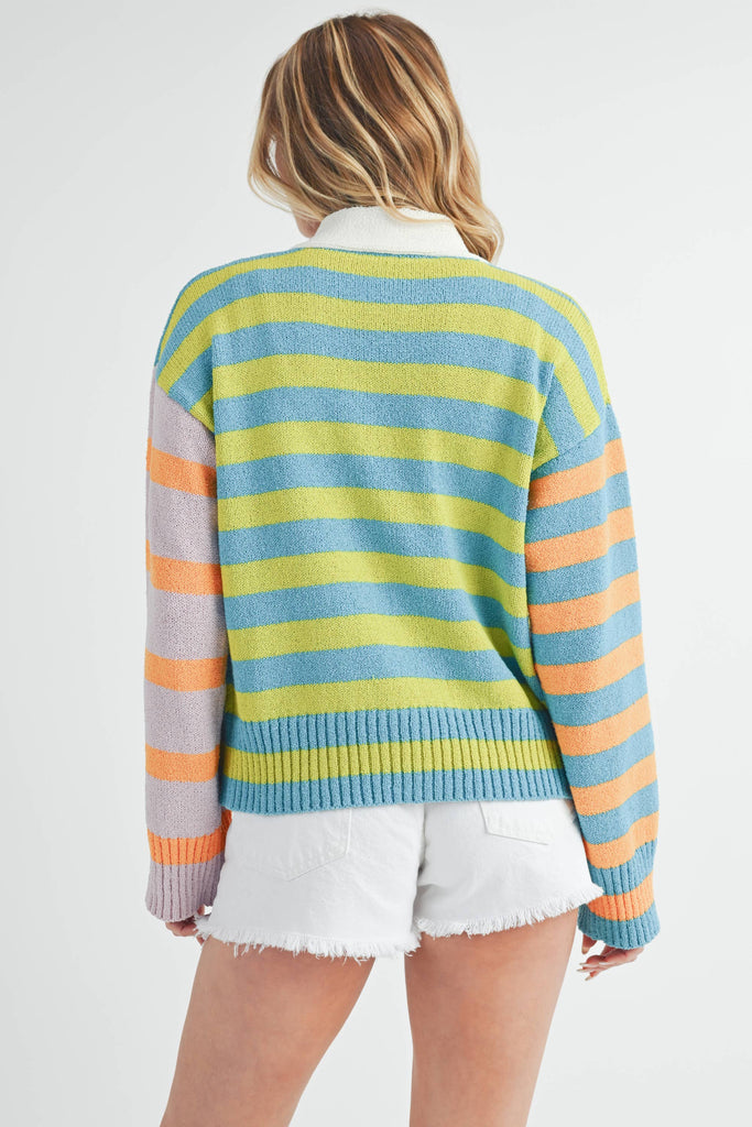 Woman wearing a colorful striped cardigan in pink, blue, green, orange, and lilac with a button-front closure.