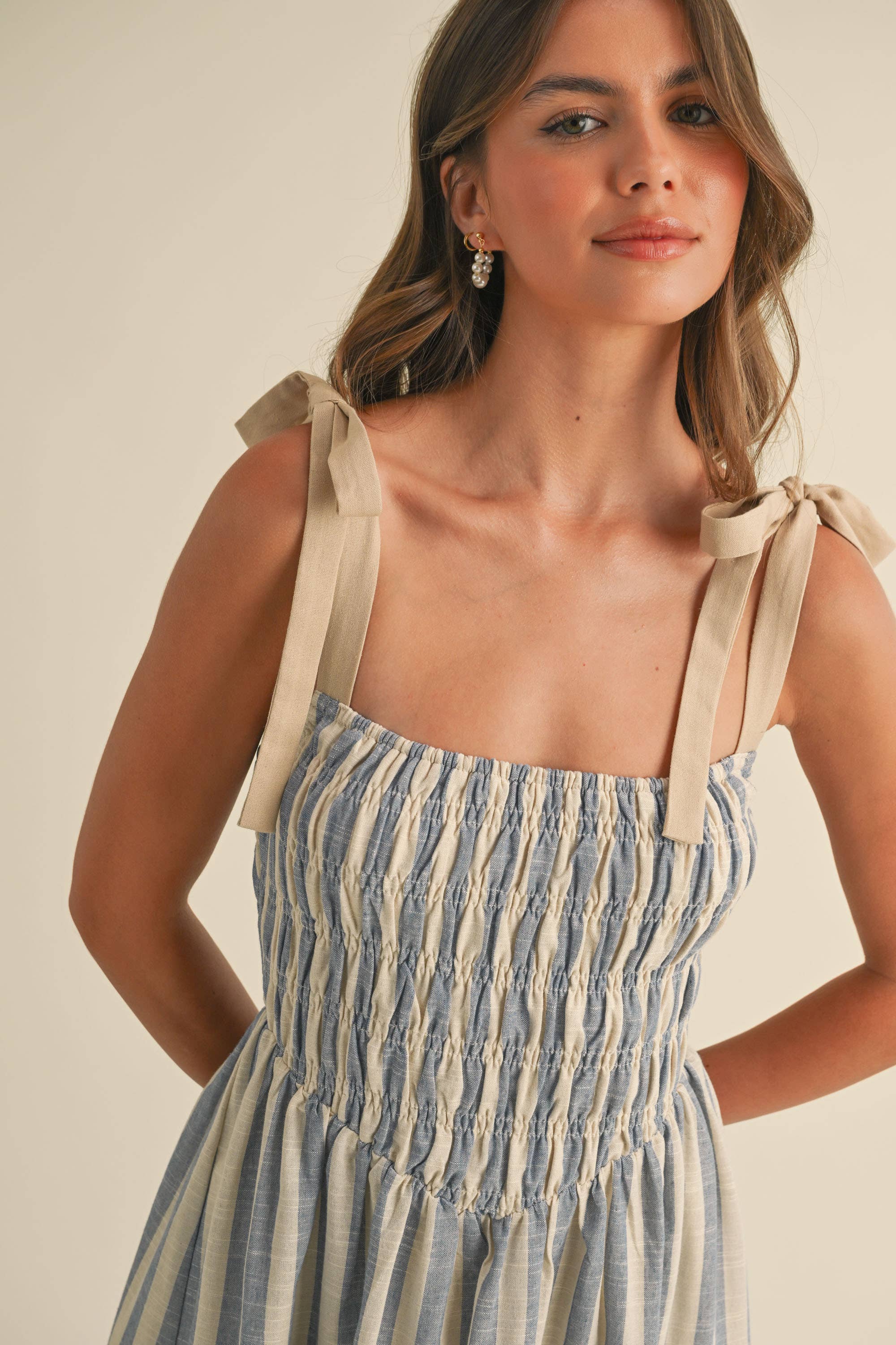Woman wearing a blue and cream striped midi dress with smocked bodice and tie shoulder straps.