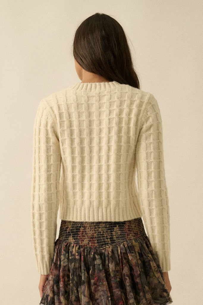 Woman wearing a cream textured knit cardigan with covered buttons, styled with a floral skirt.