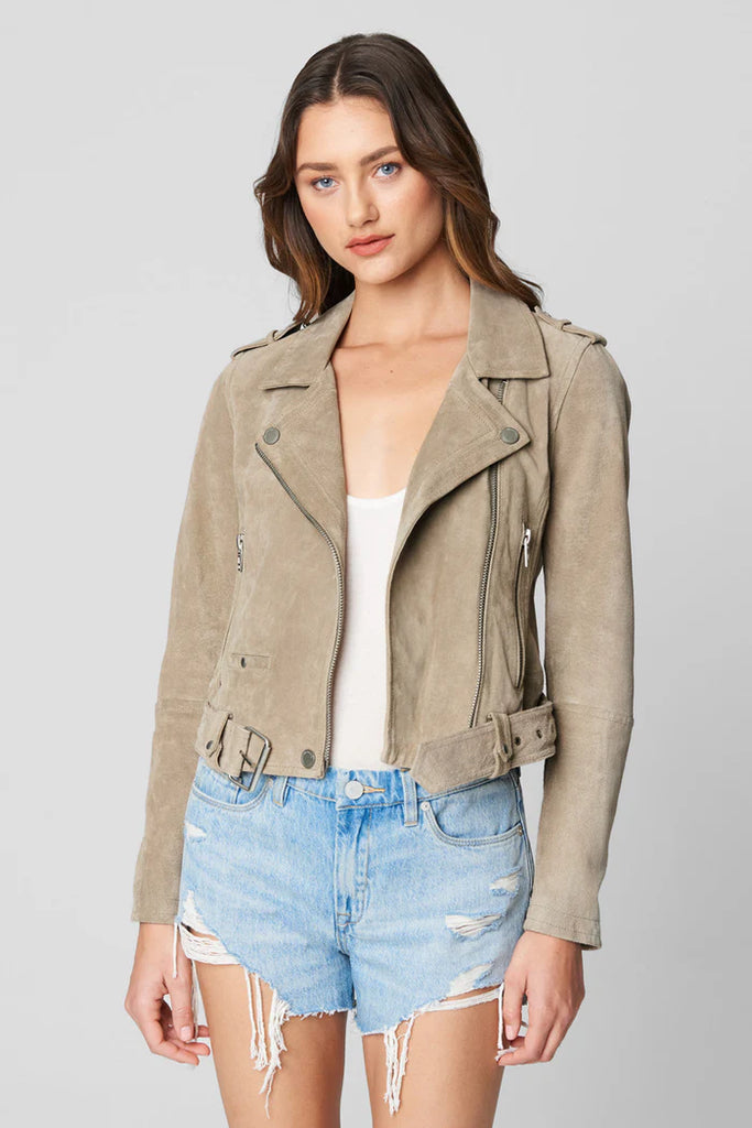 Woman wearing a beige jacket and denim shorts on a gray background