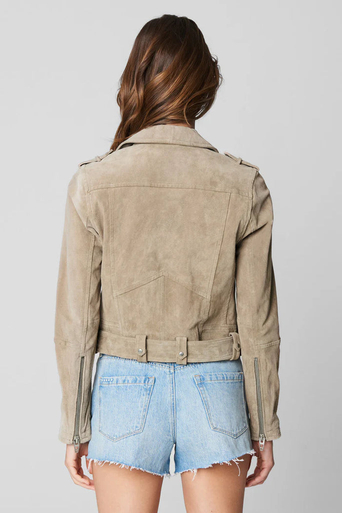 Person wearing a beige suede jacket and denim shorts on a plain background