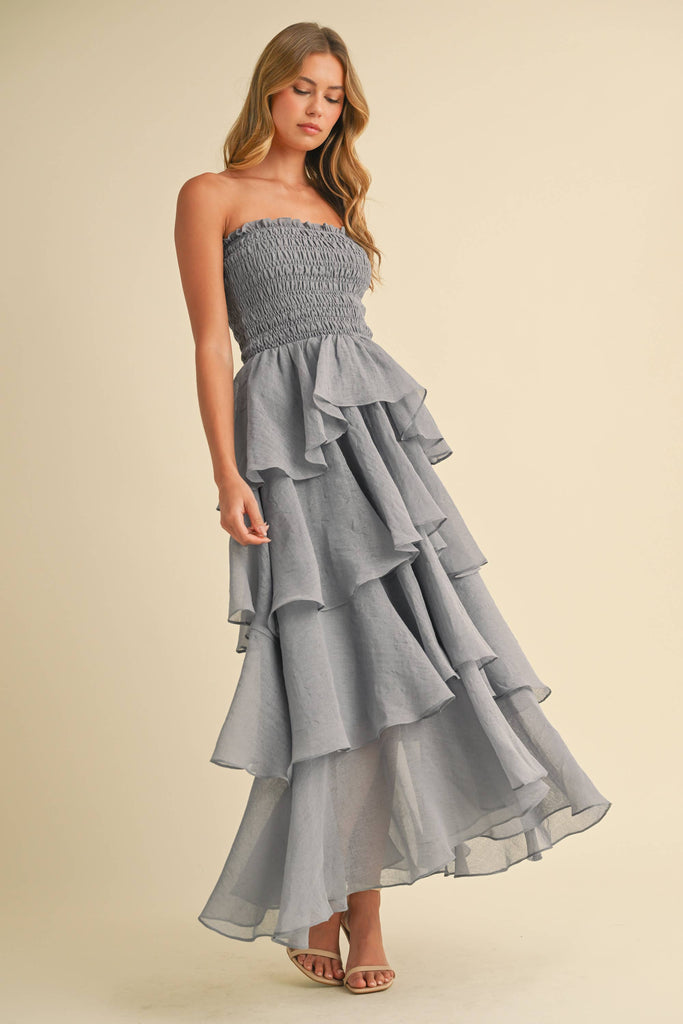 Woman wearing a strapless ruffled maxi dress with a smocked bodice, available in taupe and black.
