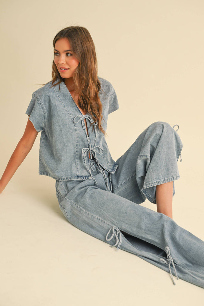 Woman wearing a light-wash denim two-piece set with tie-front top and wide-leg pants featuring side tie accents.