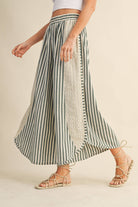 Person wearing a green and white striped skirt with lace details on a beige background
