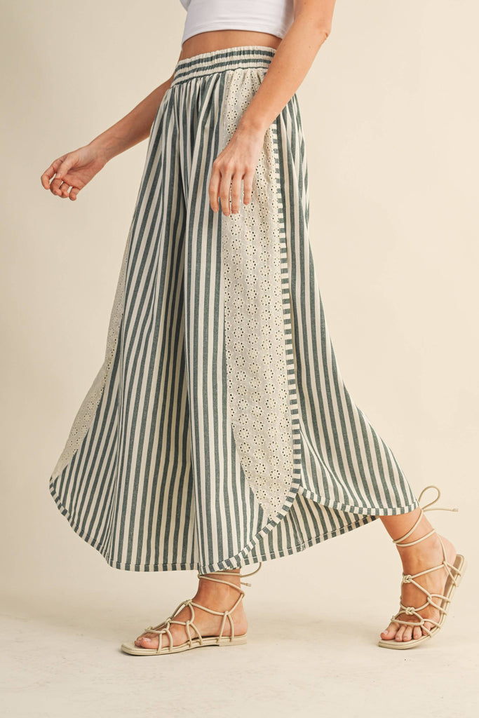 Person wearing a green and white striped skirt with lace details on a beige background