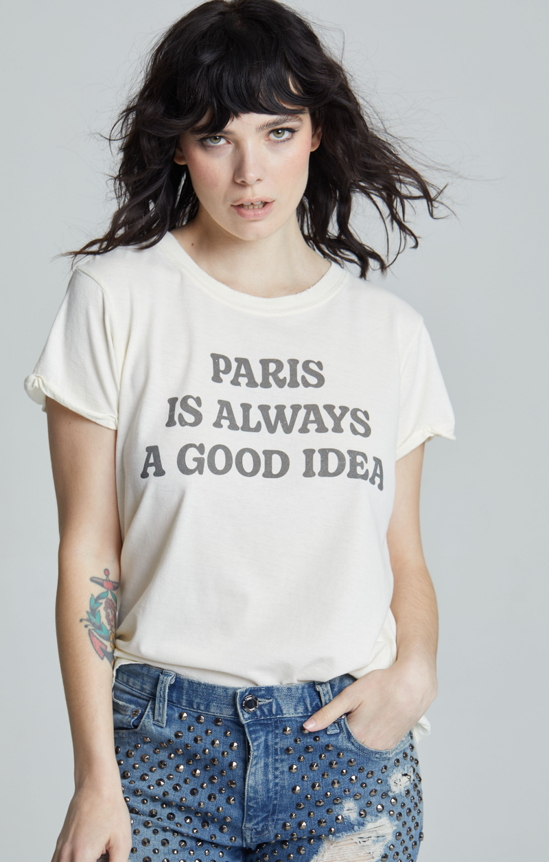Model wearing a white t-shirt with the phrase “Paris is always a good idea” printed on the front, paired with studded denim shorts.