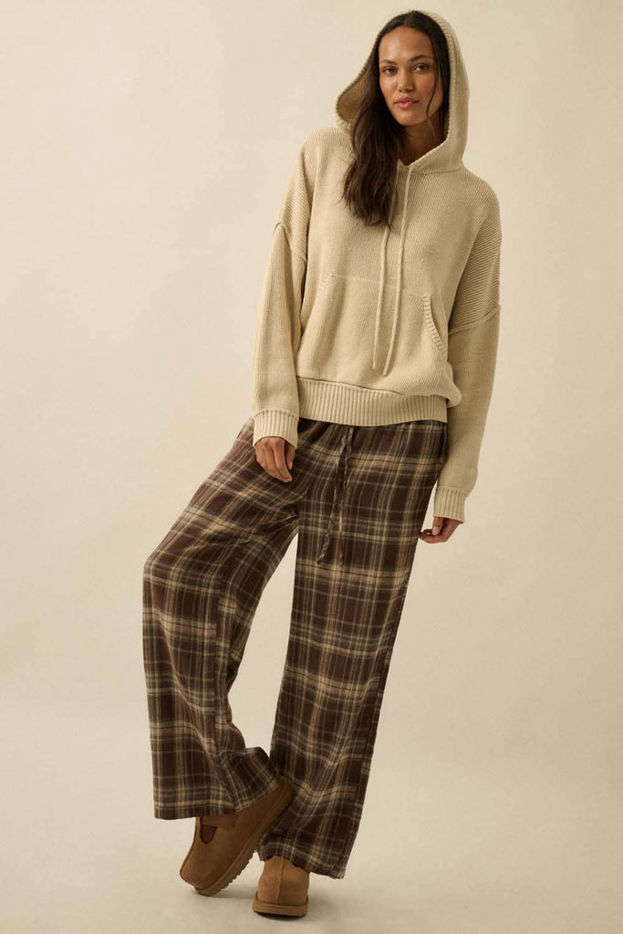 Woman wearing a beige hoodie and plaid pants on a plain background