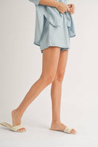 Woman wearing a white textured sleeveless button-up top and matching shorts.
