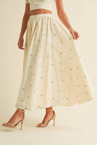 Light cream two-piece set with small floral embroidery, featuring bow-tie strap top and flowy maxi skirt