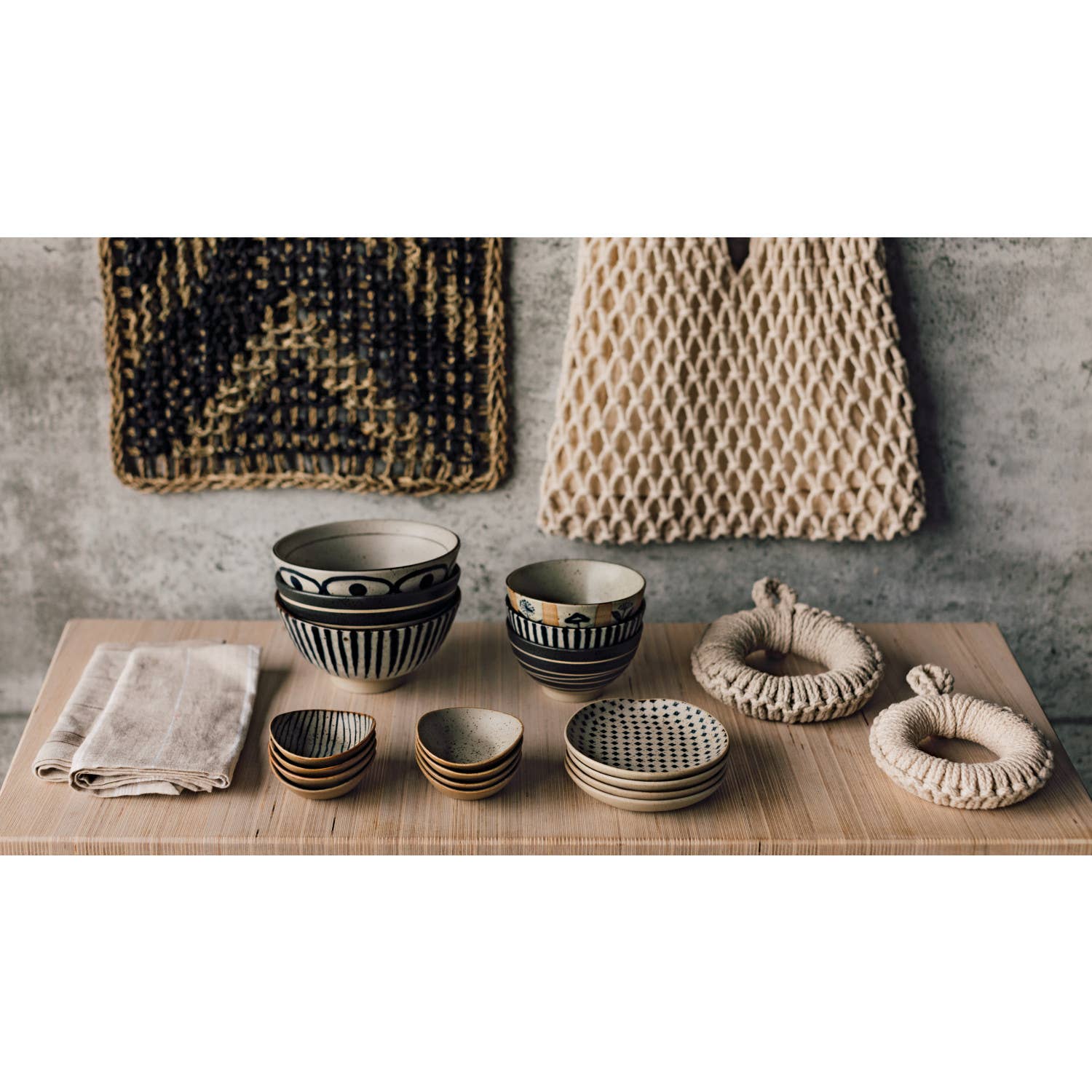 Set of ceramic bowls and woven items on a wooden surface with a textured wall background.