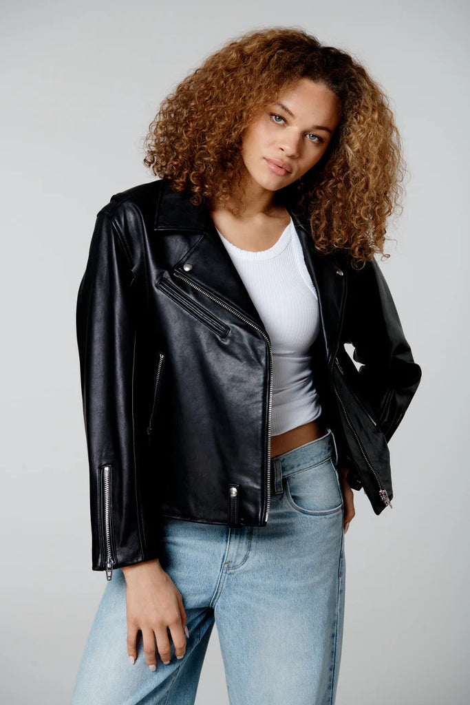 Woman wearing a black leather jacket, white top, and blue jeans on a plain background