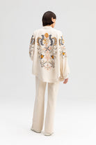 Back view of a cream-colored kimono jacket with colorful floral embroidery, worn with matching light trousers.