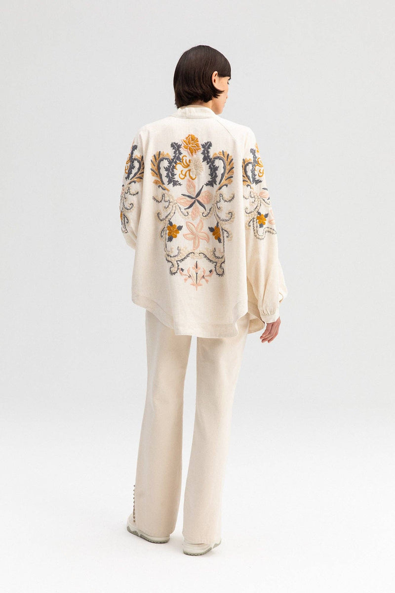 Back view of a cream-colored kimono jacket with colorful floral embroidery, worn with matching light trousers.