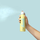 Person holding a Bask SPF 30 Sunscreen Spray against a sunny beach 