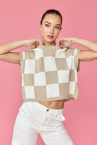 Woman wearing a beige and white loose-fit checker knit top with white pants.