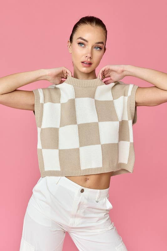 Woman wearing a beige and white loose-fit checker knit top with white pants.
