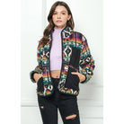 Woman wearing a multicolor fleece zip-up jacket with Southwest pattern and black contrast pockets over a lavender crop top and black ripped jeans.