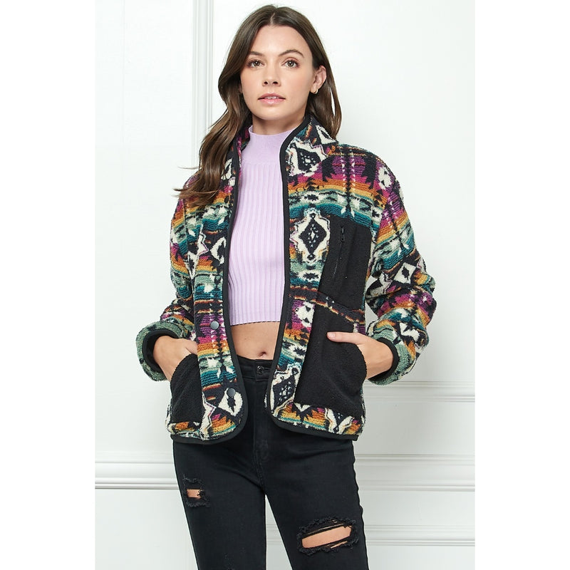 Woman wearing a multicolor fleece zip-up jacket with Southwest pattern and black contrast pockets over a lavender crop top and black ripped jeans.