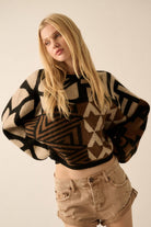 Model wearing a patterned knit sweater with bold geometric designs in neutral and contrasting tones, styled with casual bottoms.