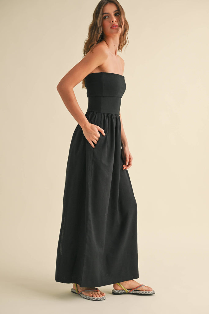 Woman wearing a black strapless maxi dress with a fitted bandeau bodice and flowy skirt.