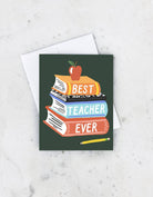 Greeting card with stacked books reading "Best Teacher Ever," apple and pencil illustration on a dark green background.