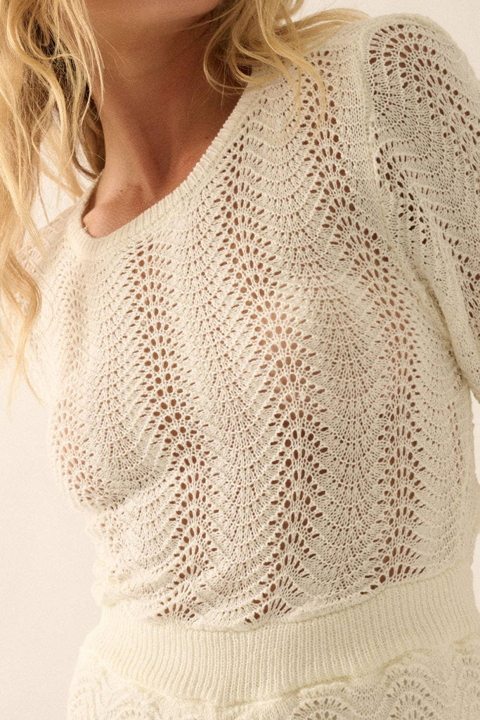 Woman wearing a beige knit romper with bell sleeves, scalloped hems, and open-weave detailing.