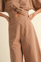 Woman wearing a two-piece striped set with a twist-front crop top and wide-leg pants in cream and tan color options.