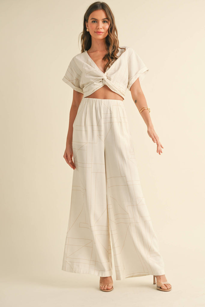 Woman wearing a cream two-piece set with geometric line print, knotted crop top, and wide-leg pants.