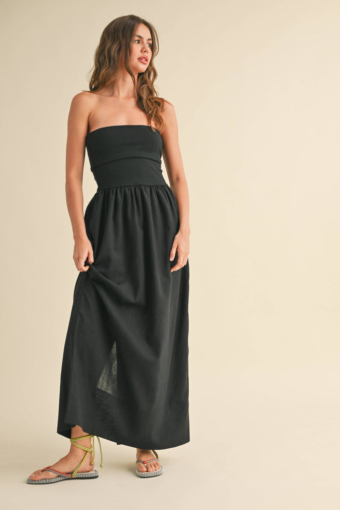 Woman wearing a black strapless maxi dress with a fitted bandeau bodice and flowy skirt.