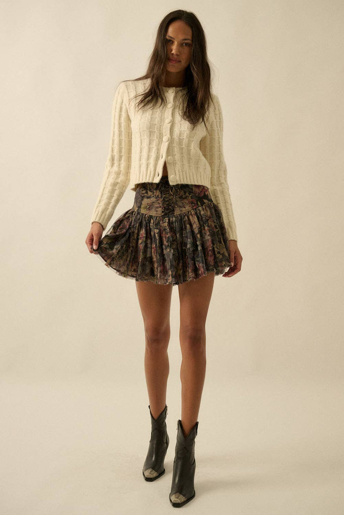 Woman wearing a cream textured knit cardigan with covered buttons, styled with a floral skirt.