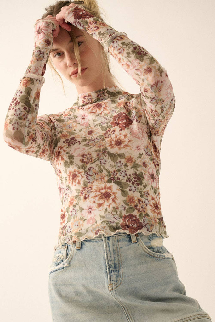 Woman wearing a sheer mesh floral long-sleeve top with mock neck and fitted silhouette.