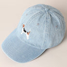 Light blue denim cap with embroidered dog design on a beige background