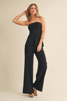 Woman wearing a black strapless jumpsuit on a beige background