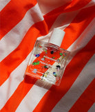 Poom Poom Eau de Parfum bottle with playful illustrations, displayed on an orange and white striped fabric background.
